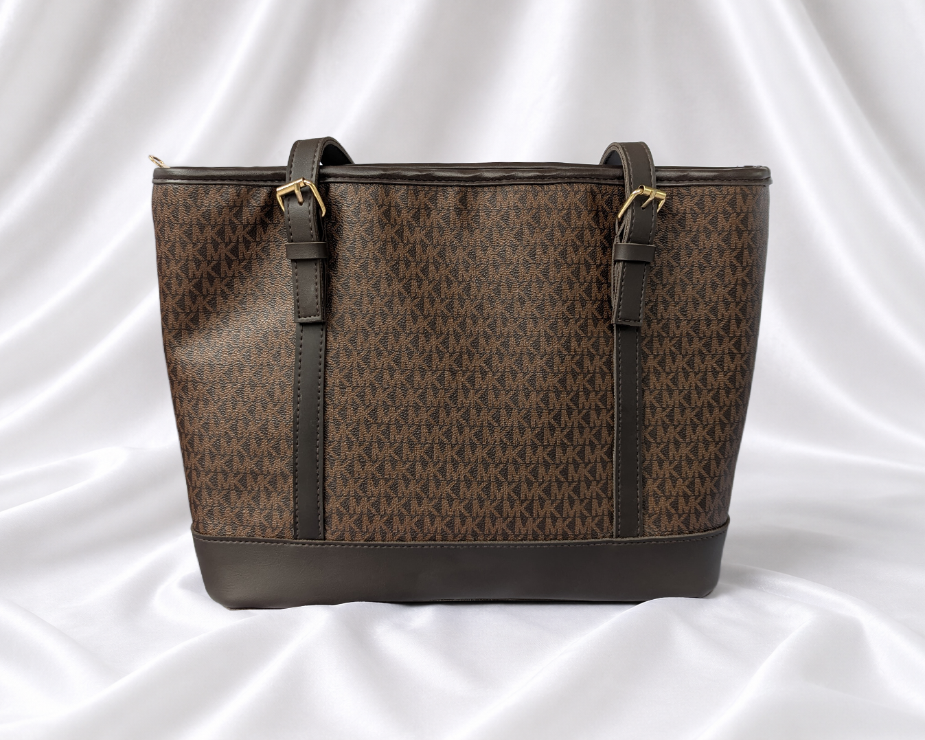 Brown women's monogram-inspired tote bag with dual shoulder straps and gold-tone buckle details.