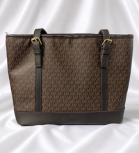 Brown women's monogram-inspired tote bag with dual shoulder straps and gold-tone buckle details.